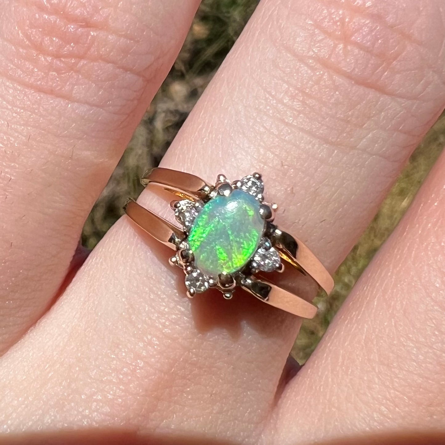 Close-up of women's 14k gold green Australian opal and diamond ring, worn on finger in natural light