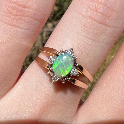 Close-up of women's 14k gold green Australian opal and diamond ring, worn on finger in natural light