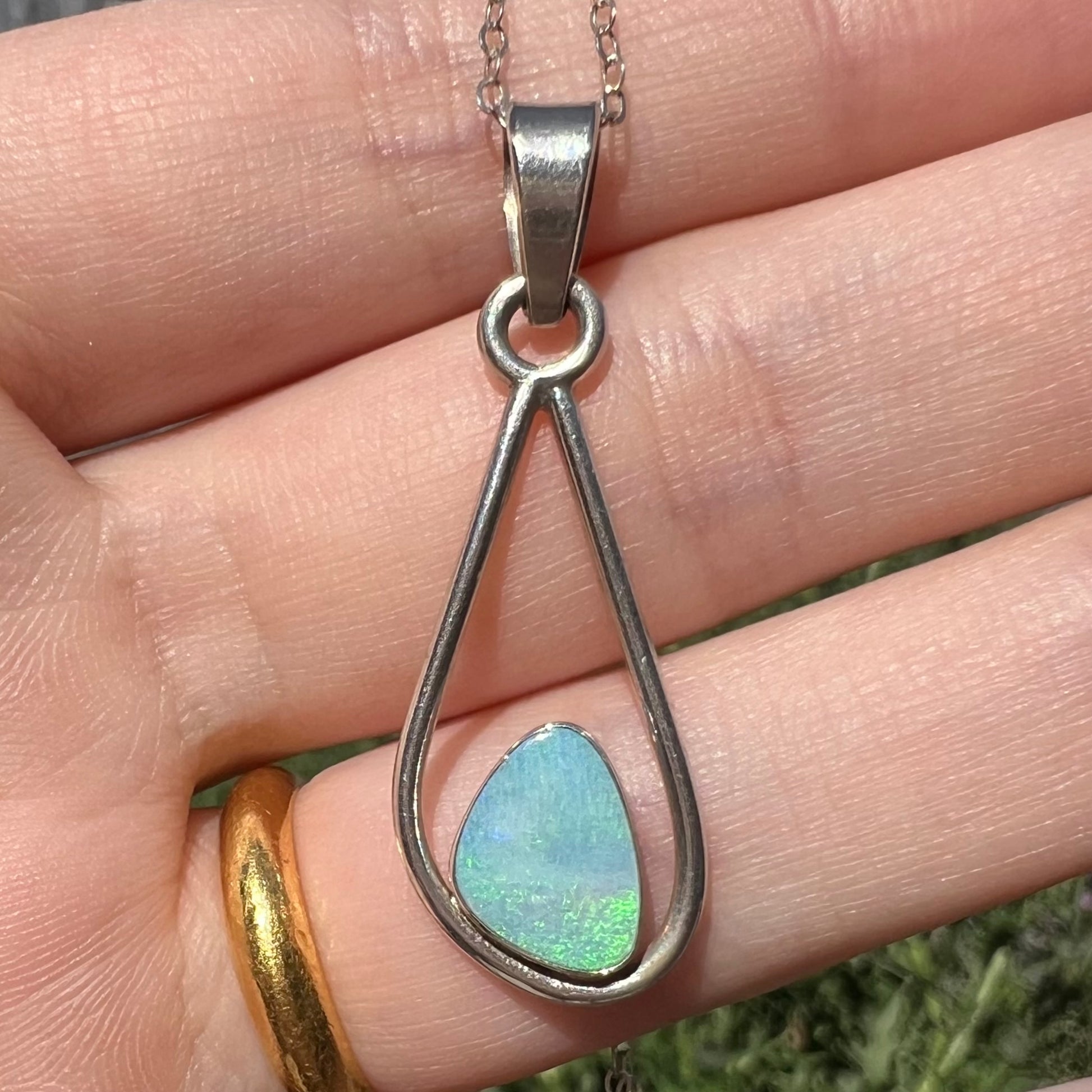 Close-up of an Australian opal doublet pendant with green play of color held in a hand under natural light.