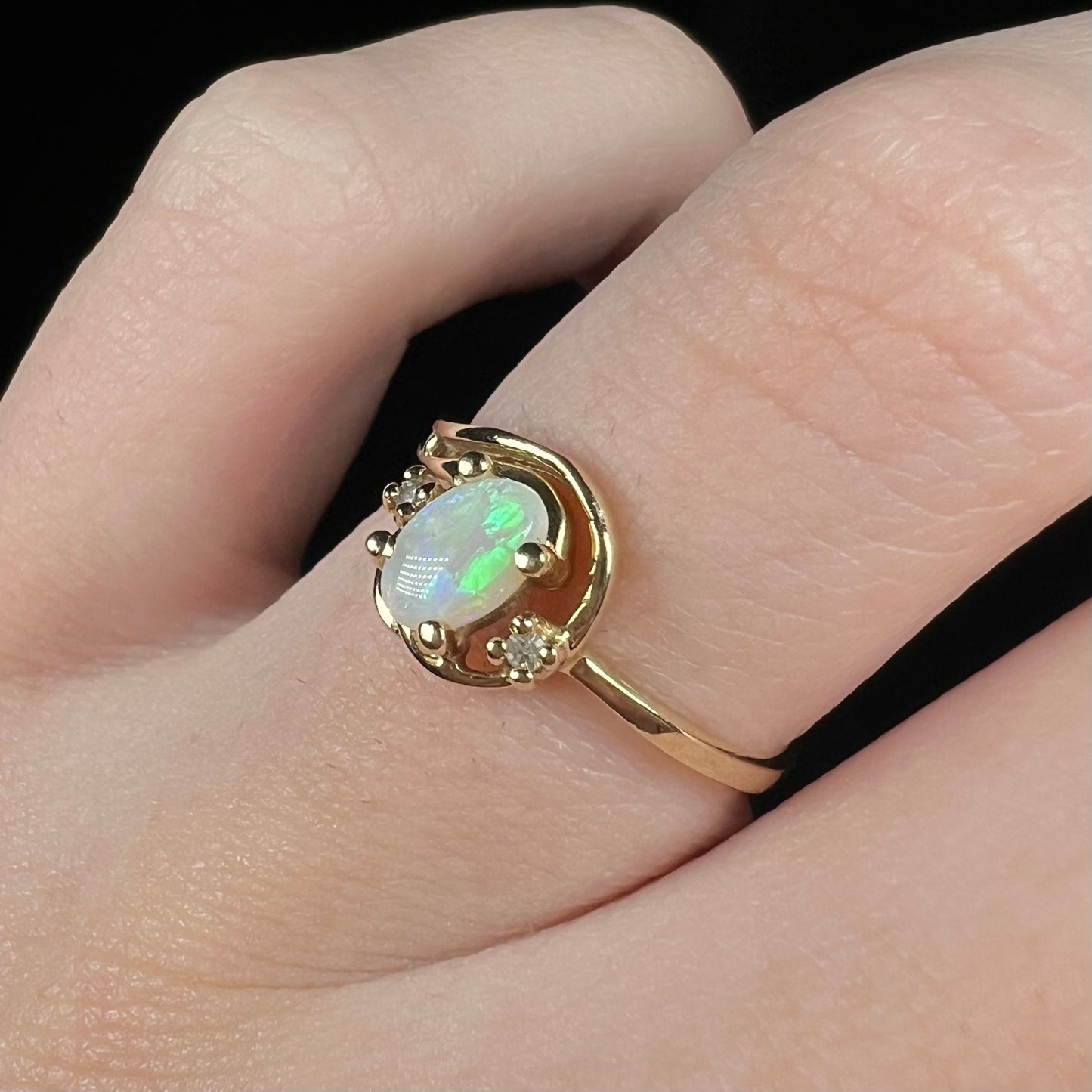 A 10k yellow gold Australian opal ring with green flashes of color shown close-up from an angle on a finger.