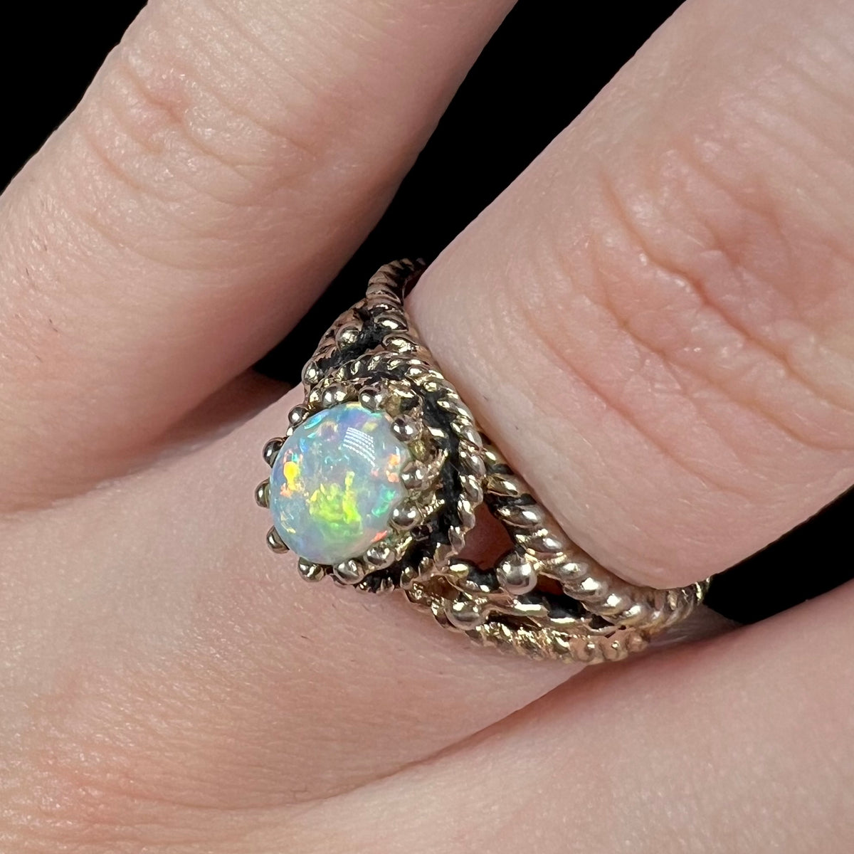 Green flashes seen in Australian opal, mounted in an estate brass ring mounting, worn on a finger and viewed close-up from angle