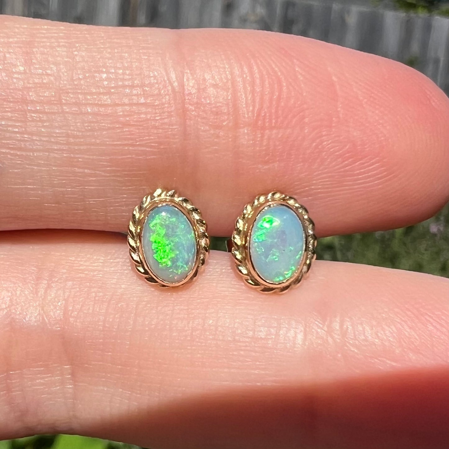 Macro close-up of green Australian opal stud earrings held between two fingers in natural light.