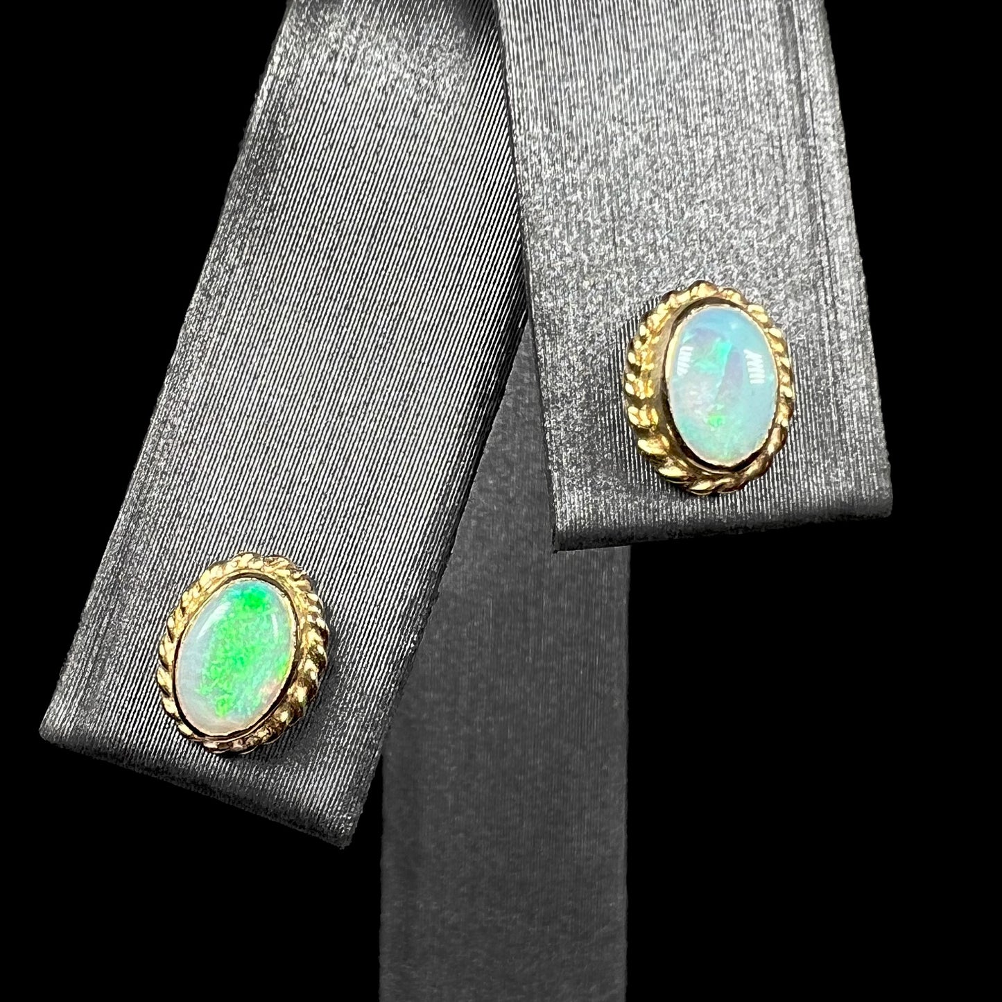 Pair of green Australian opal stud earrings in yellow gold shown from front on earring display against black background.