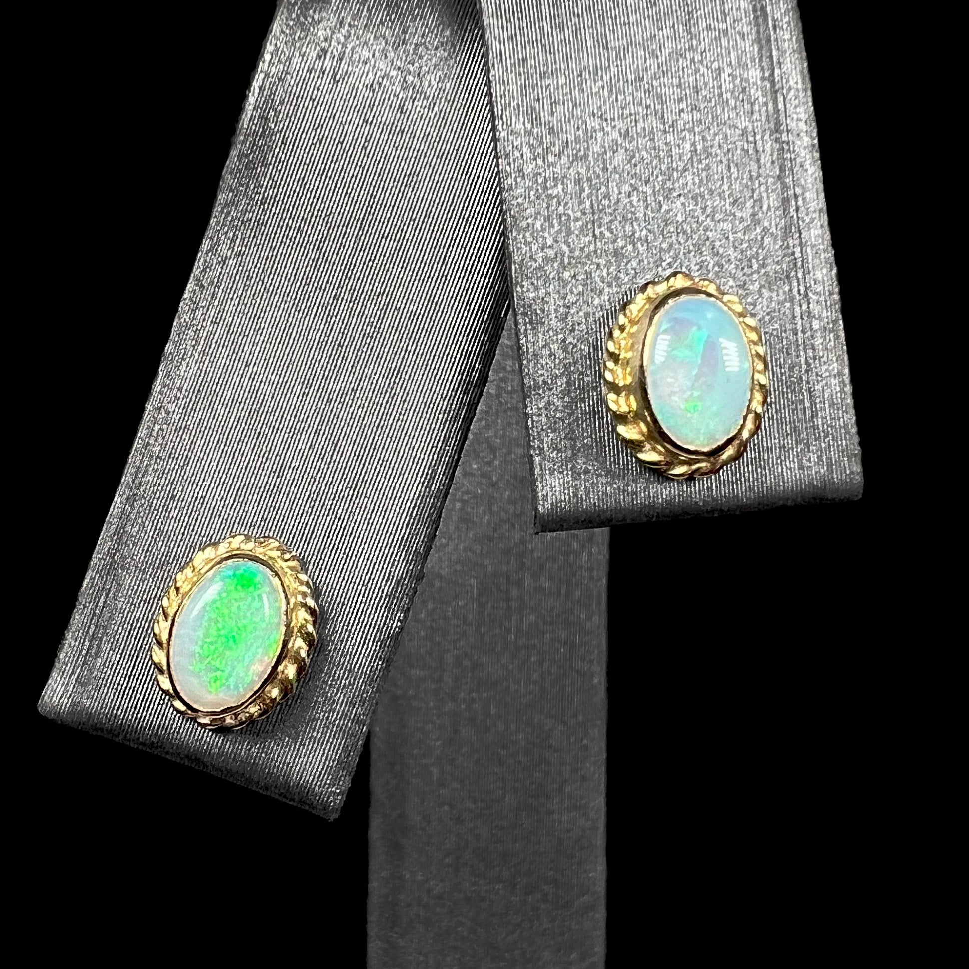 Pair of green Australian opal stud earrings in yellow gold shown from front on earring display against black background.