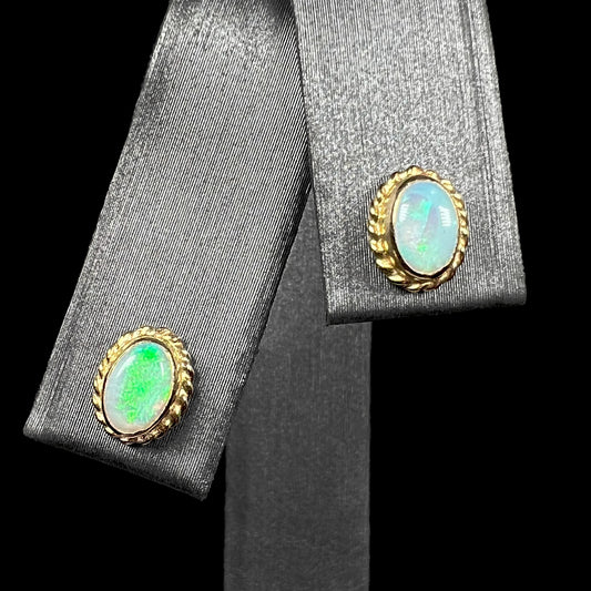 Pair of green Australian opal stud earrings in yellow gold shown from front on earring display against black background.
