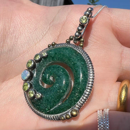 A men's aventurine koru necklace, accented with opal and peridot, shown in the sunlight from an angle.
