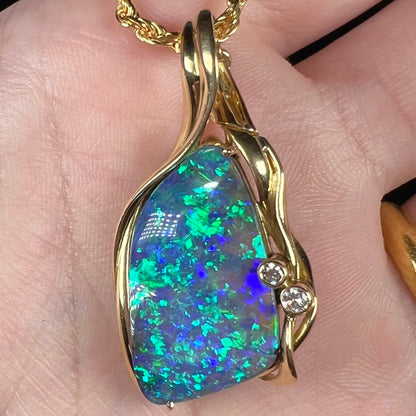 Close-up macro view of Australian boulder opal and diamond pendant with green-blue fire, held in hand.