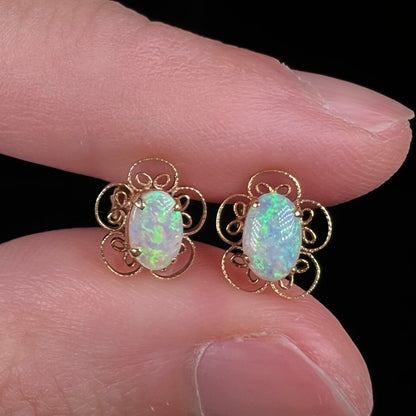 Close-up of opal flower design earrings in 14k gold with green and blue play of color, held between fingers