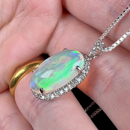 A crystal opal and diamond halo pendant made from platinum, shown from an angle in a hand.  The opal has subtle green play of color.