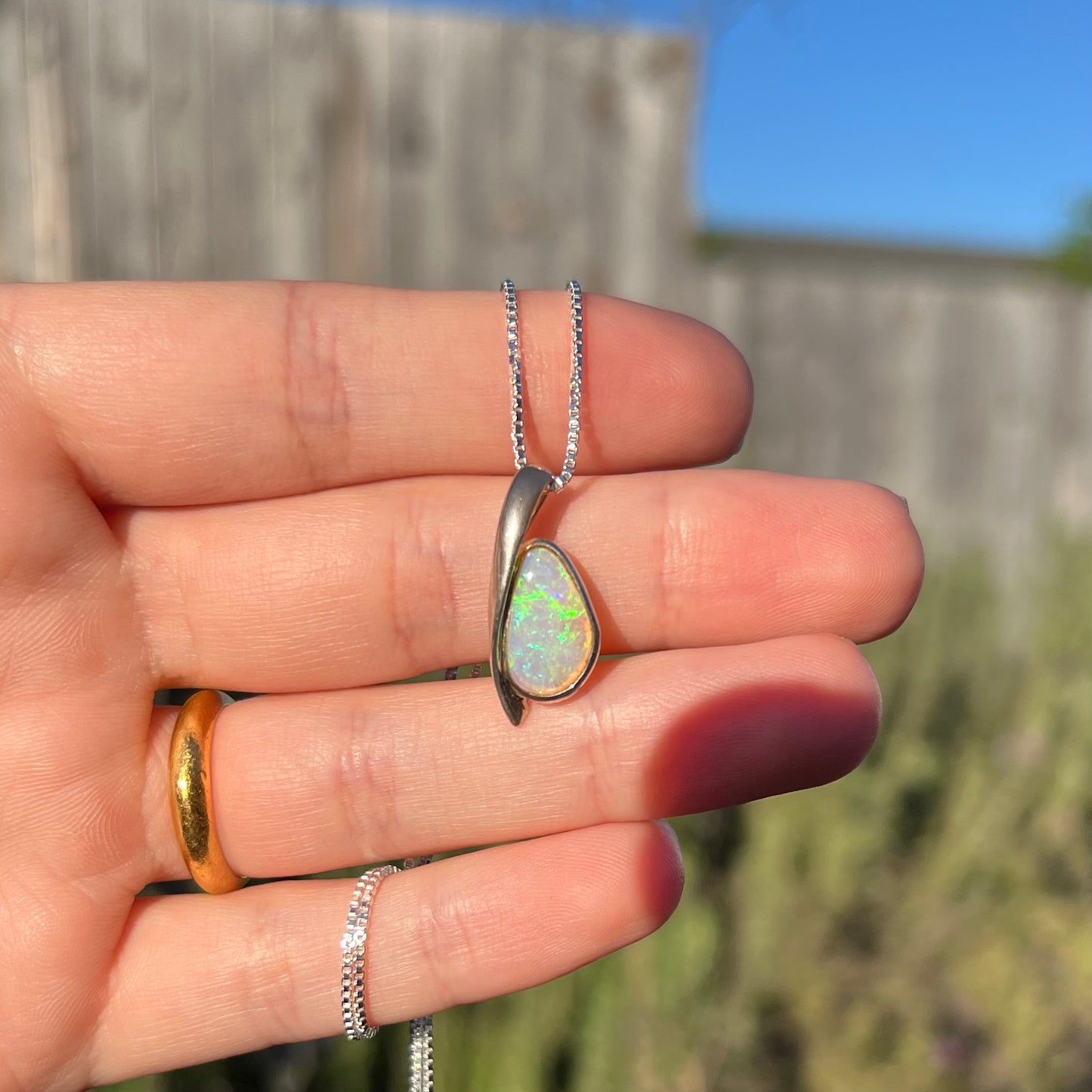A green Australian crystal opal necklace in sterling silver shown held in a hand in the sunight against an outdoor background.