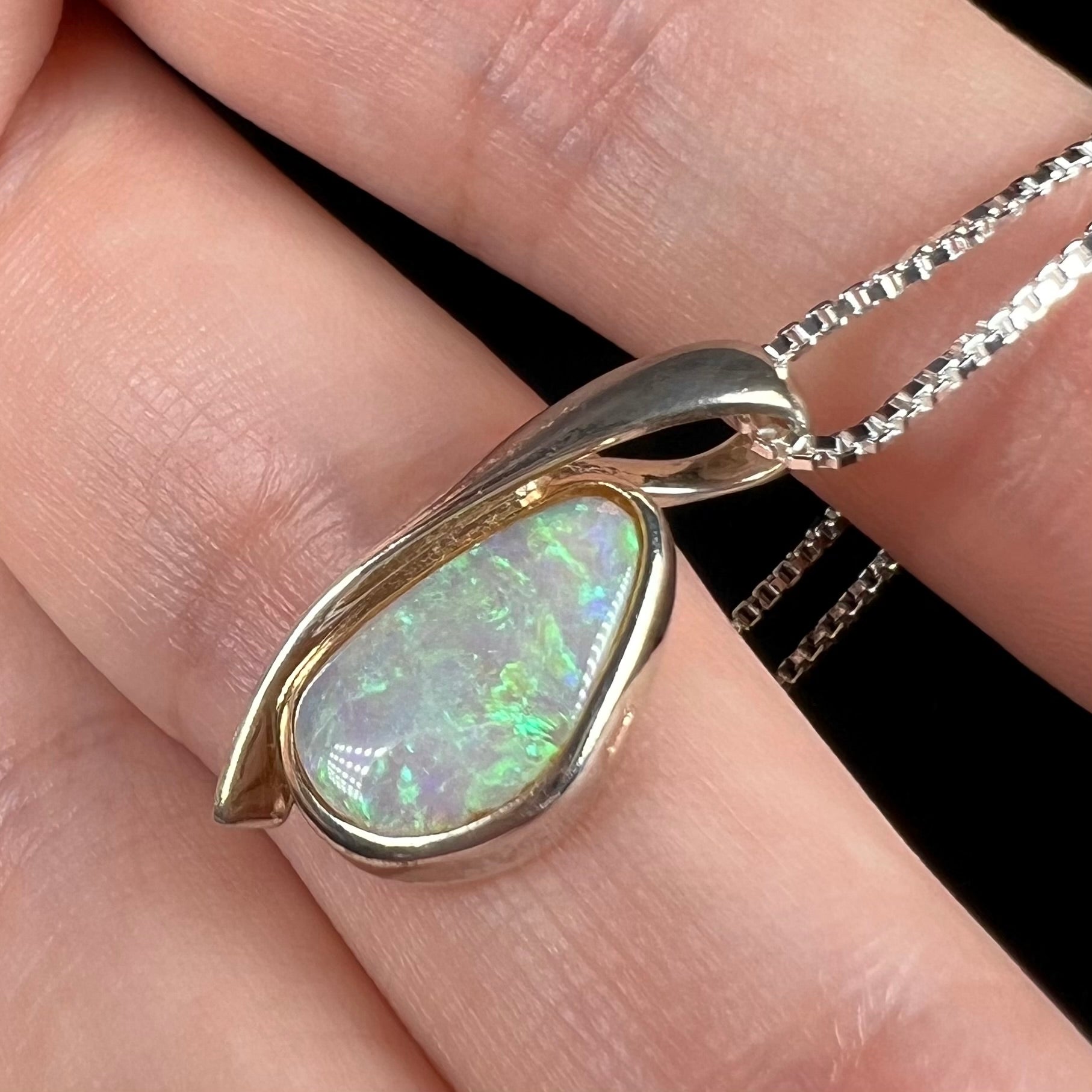 A green Australian crystal opal pendant in sterling silver shown close-up in a hand from an angle.