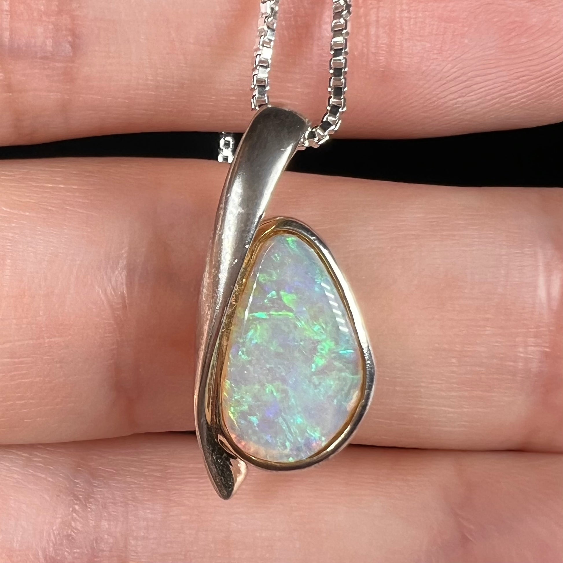 A green Australian crystal opal pendant in sterling silver shown close-up in a hand against a black background.