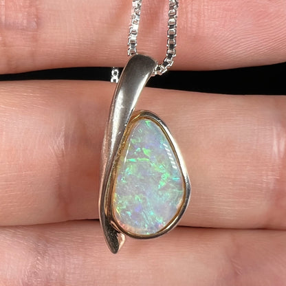 A green Australian crystal opal pendant in sterling silver shown close-up in a hand against a black background.