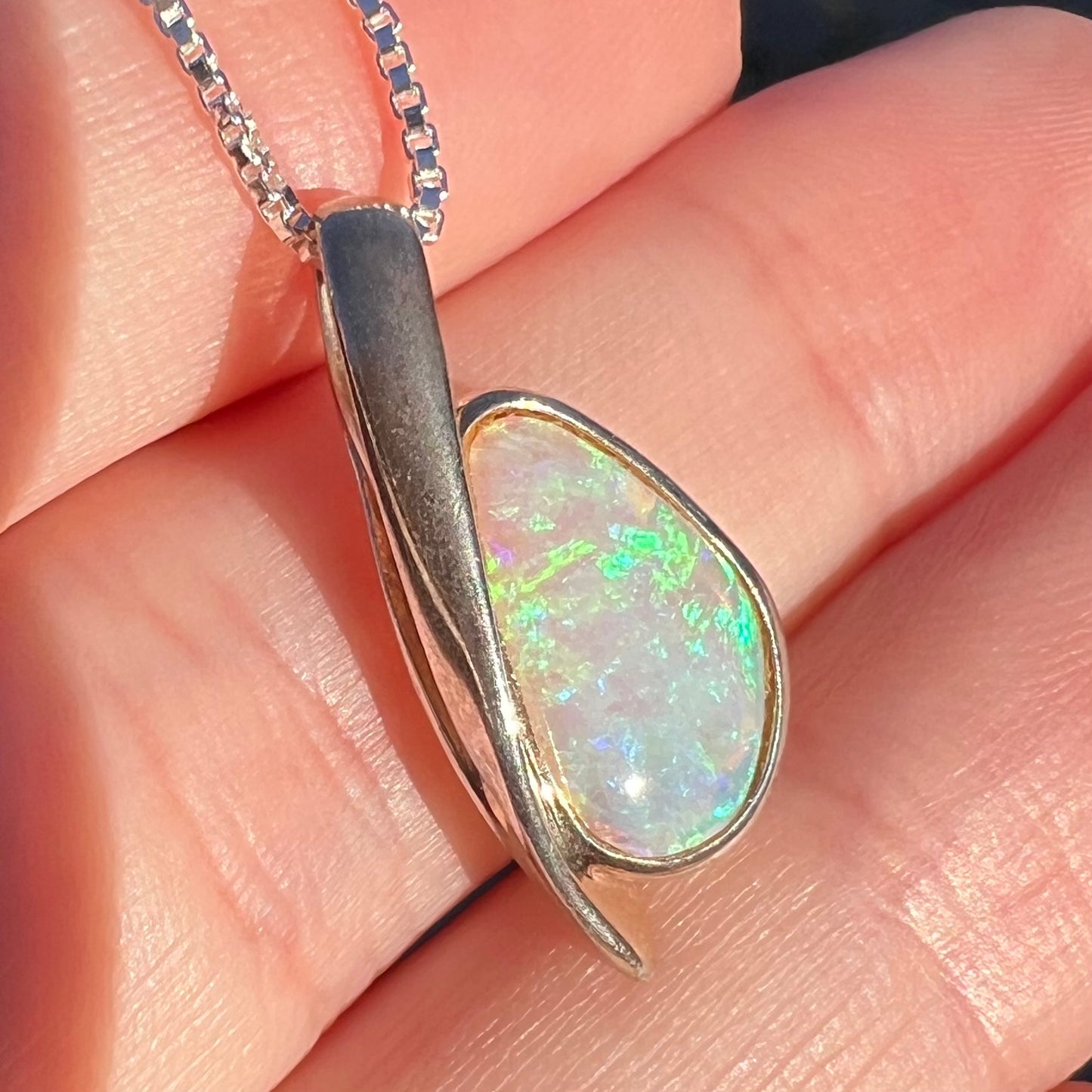 Sunlit angled close-up of a green Australian crystal opal pendant in sterling silver shown held in a hand.
