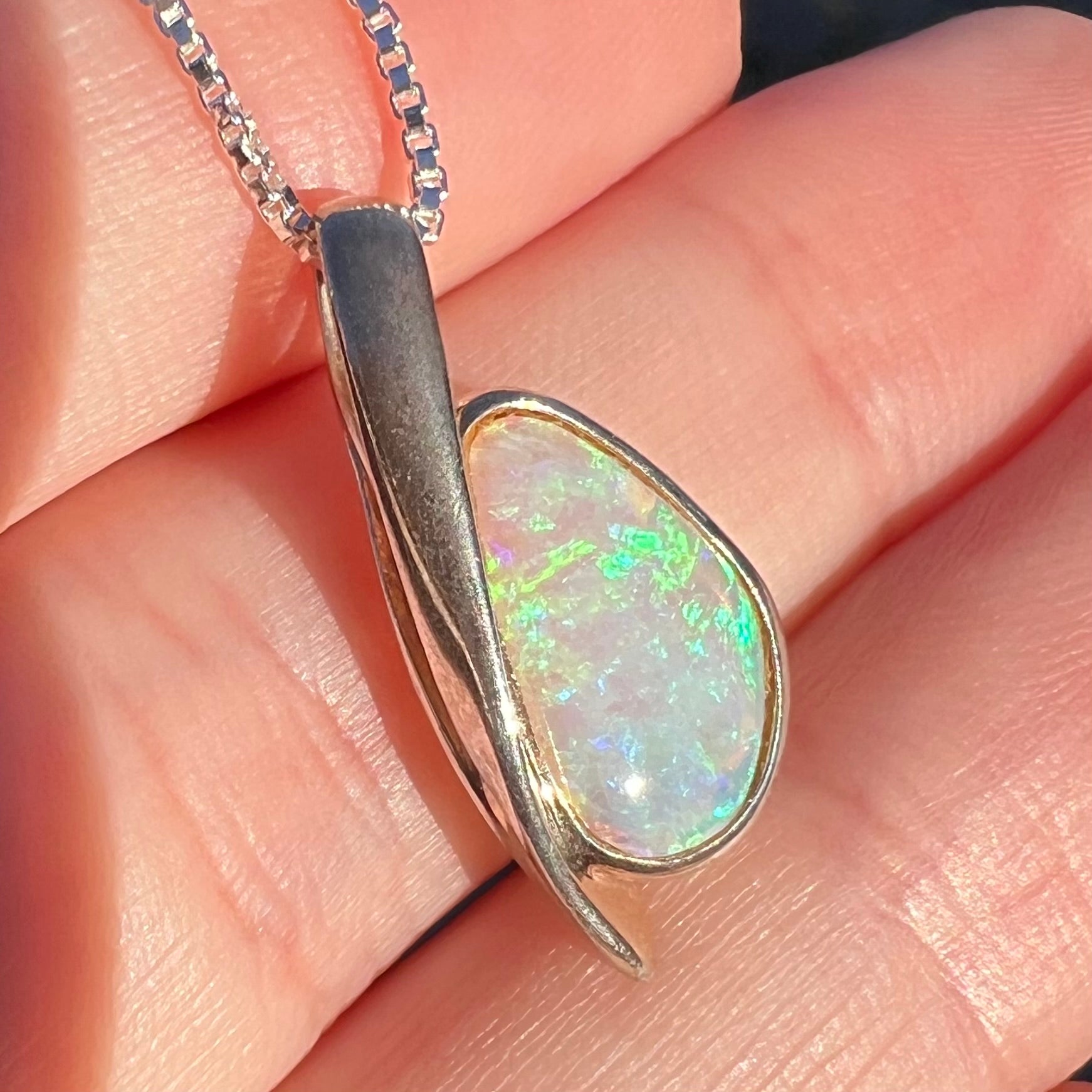 Sunlit angled close-up of a green Australian crystal opal pendant in sterling silver shown held in a hand.