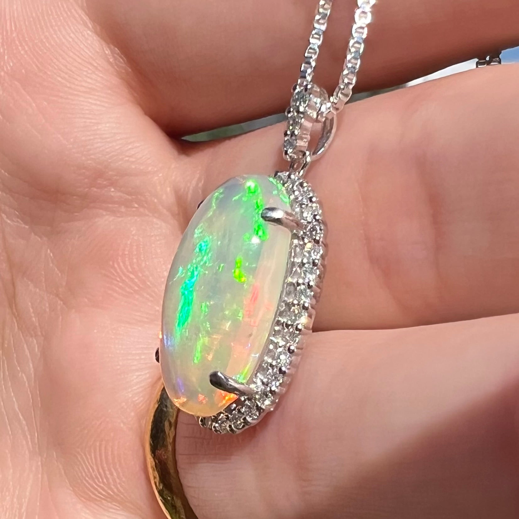 Angled close-up sunlit view of a green Ethiopian opal and diamond platinum pendant held in a hand.
