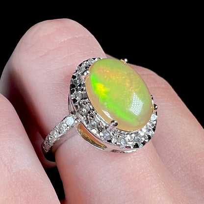 Green color play shines in a sterling silver Ethiopian fire opal ring with a CZ halo, pictured on a hand at an angled view.