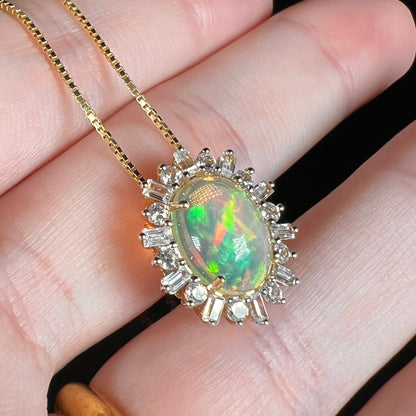 Angled close-up of Ethiopian opal pendant in 14k yellow gold, held in hand on chain.  The opal has broad green fire with red flash.