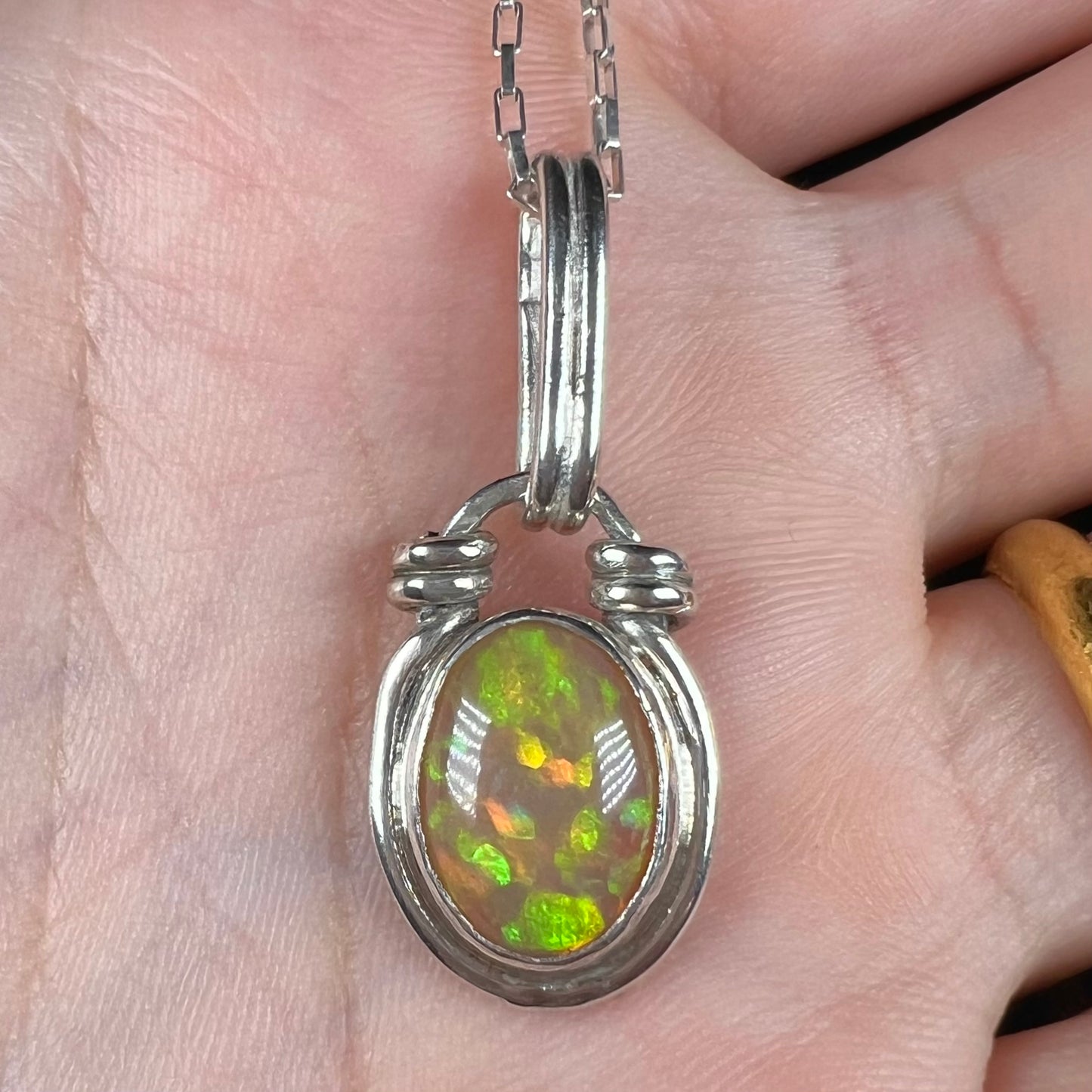 A colorful sterling silver Ethiopian opal pendant shown close-up in a hand.  The opal has green color play.