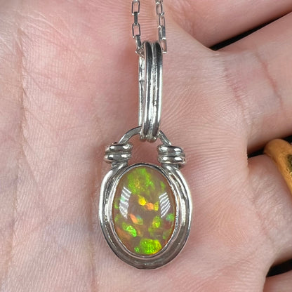 A colorful sterling silver Ethiopian opal pendant shown close-up in a hand.  The opal has green color play.