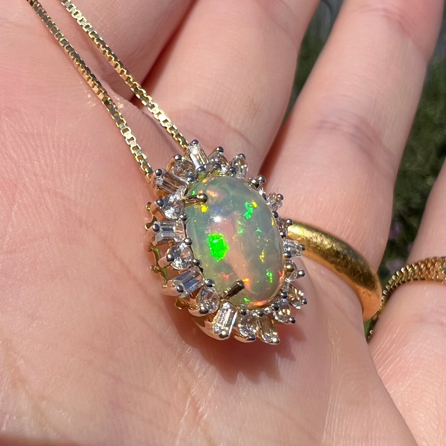 Angled close-up of yellow gold Ethiopian opal slide pendant in hand.  The opal has brilliant green flashes in sunlight.