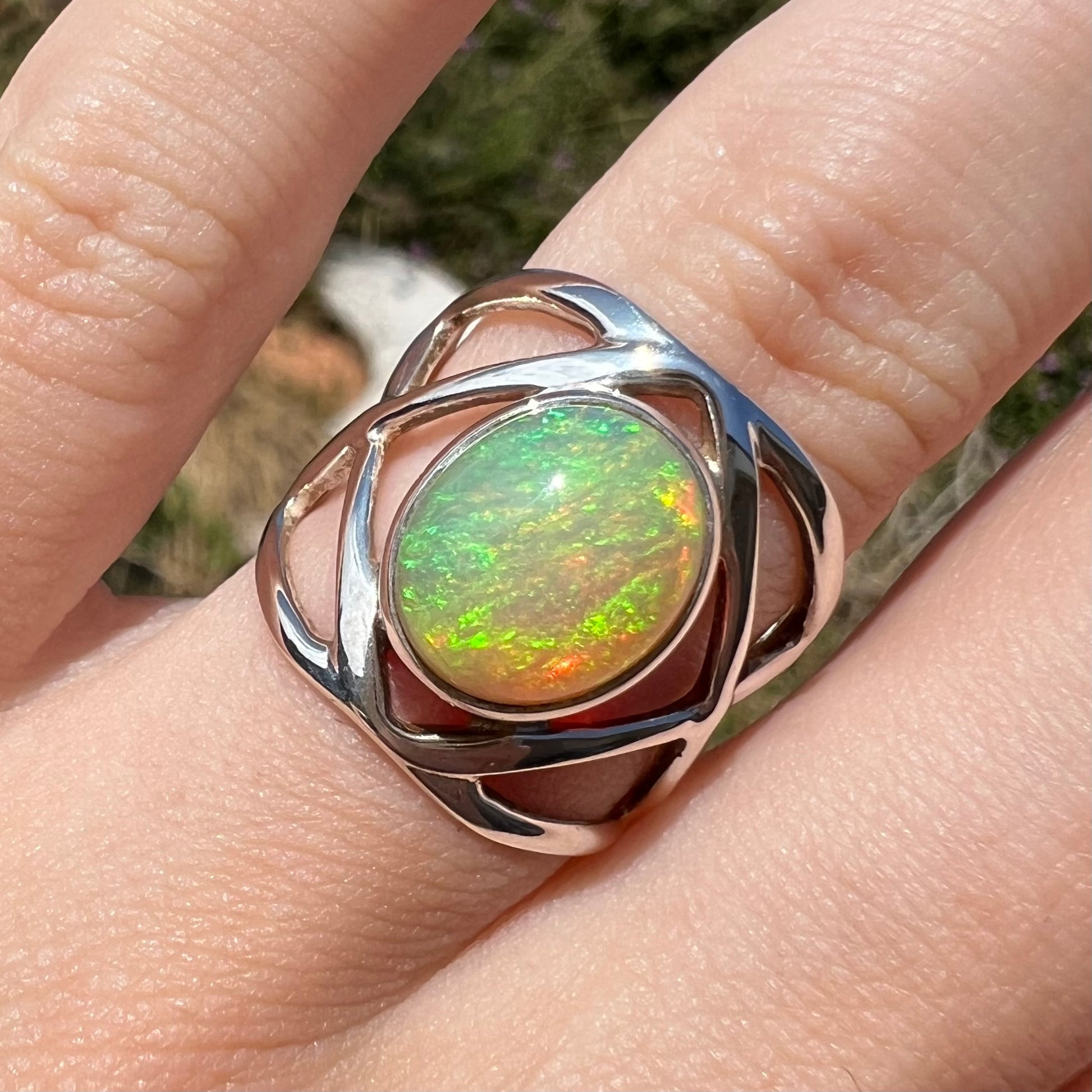 Front close-up of a green Ethiopian opal ring in silver, worn on a finger in natural light.