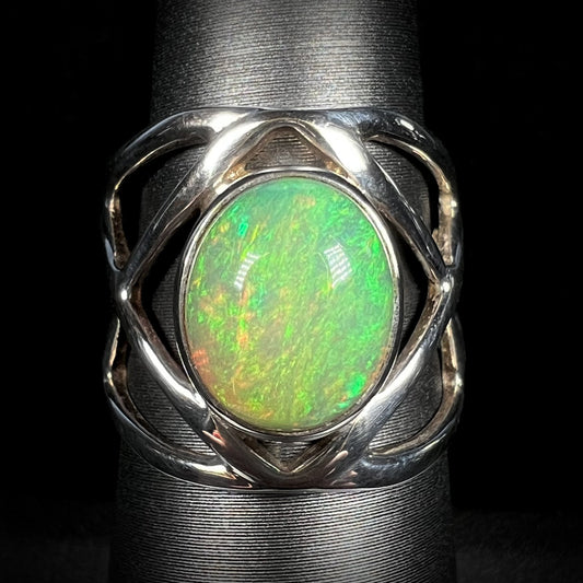 Close-up of a green Ethiopian opal ring with an open silver design shown from the front against black background.