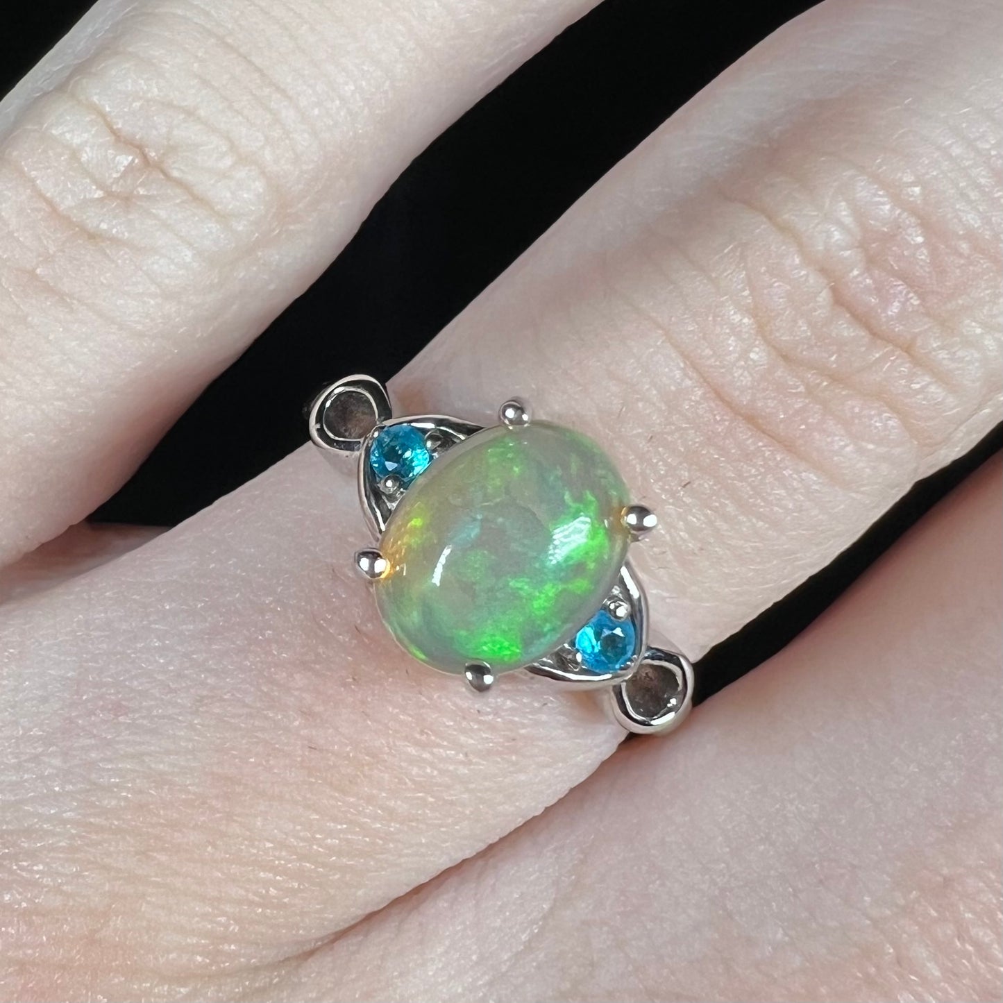 Close-up of green Ethiopian opal ring with two round blue apatite accents on finger