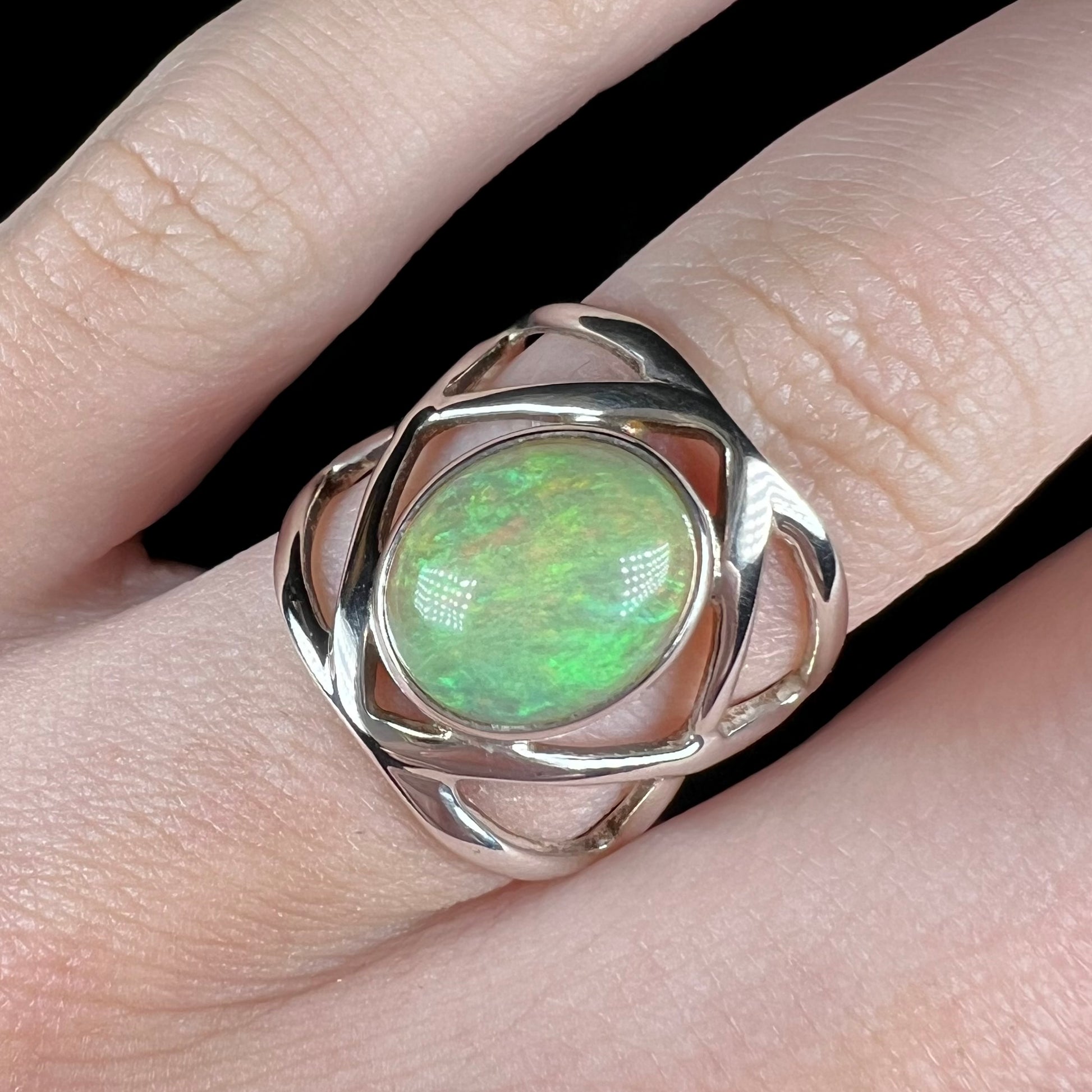 A green Ethiopian opal ring worn on a finger, shown close-up worn on a finger from the front in LED light.
