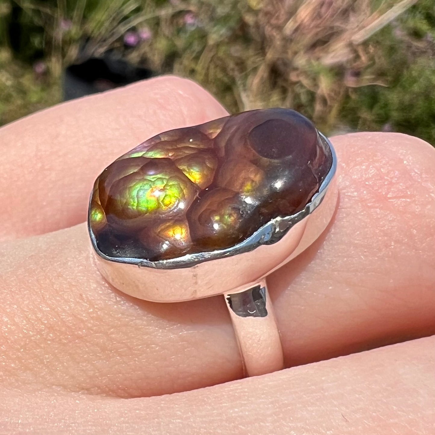A sterling silver Mexican fire agate ring with green iridescence shown at an angle on a hand in sunlight.
