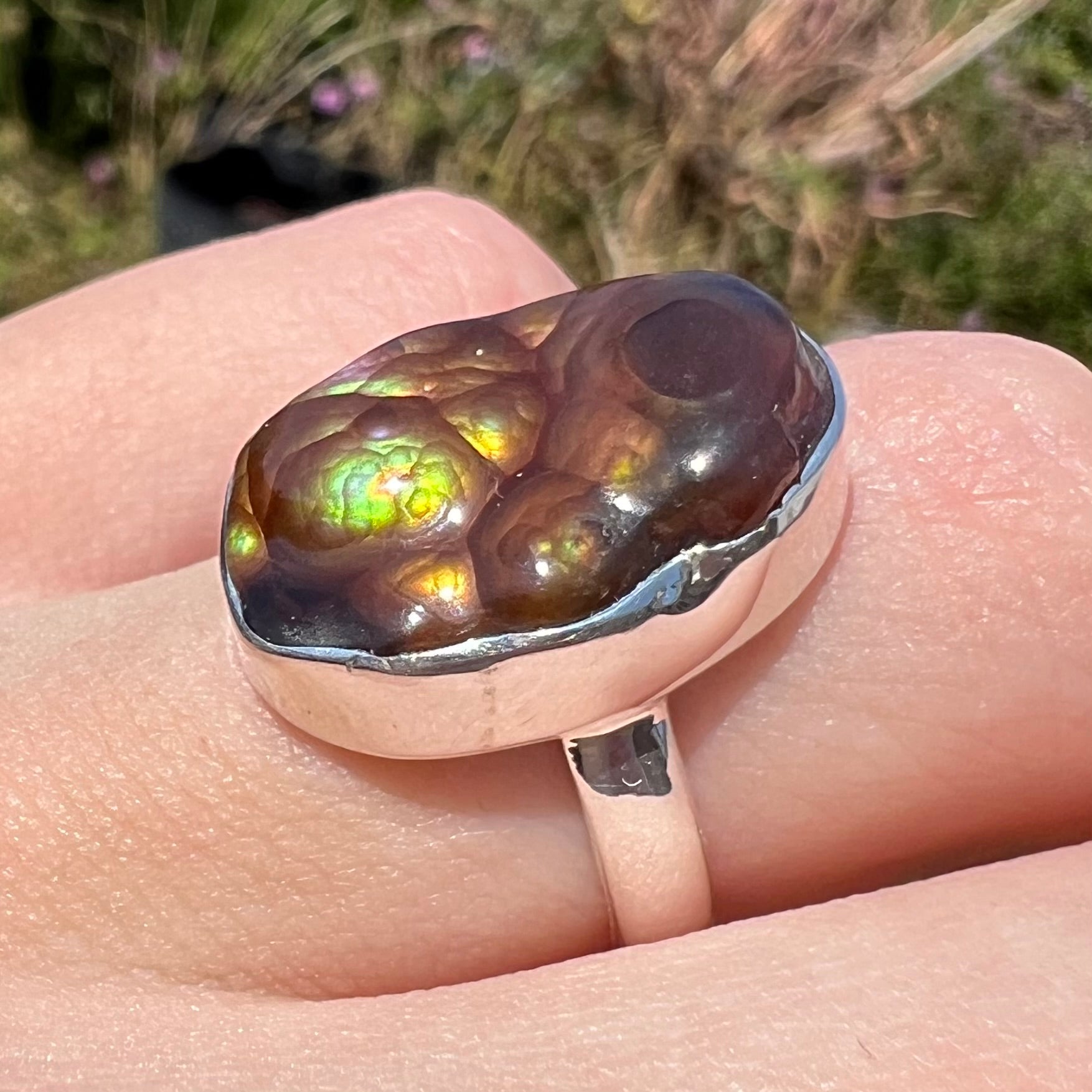 A sterling silver Mexican fire agate ring with green iridescence shown at an angle on a hand in sunlight.