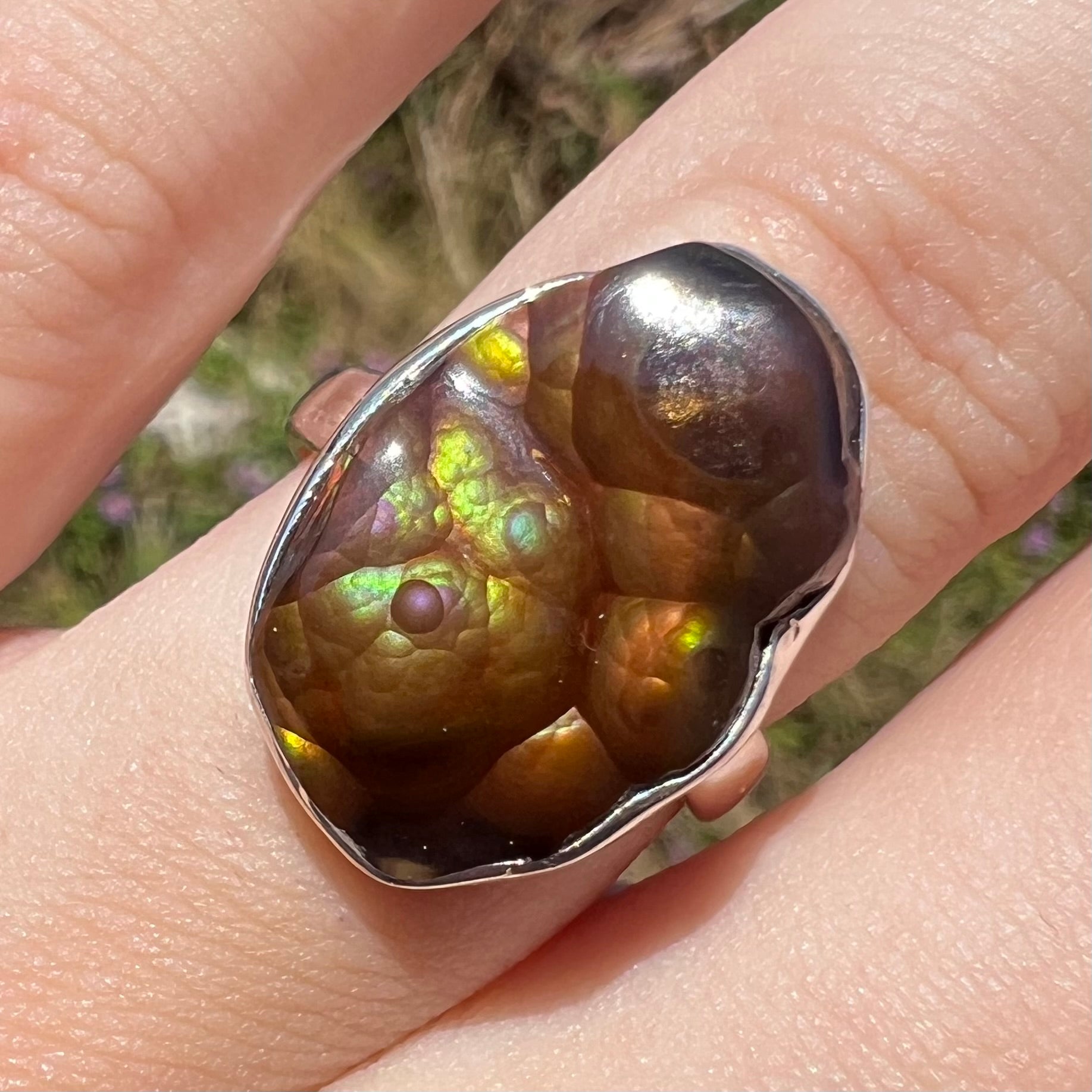 Front of a sterling silver Mexican fire agate ring with green and purple iridescence shown close-up in sunlight.