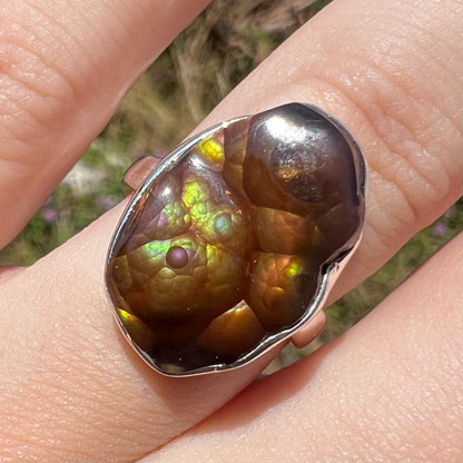 Front of a sterling silver Mexican fire agate ring with green and purple iridescence shown close-up in sunlight.