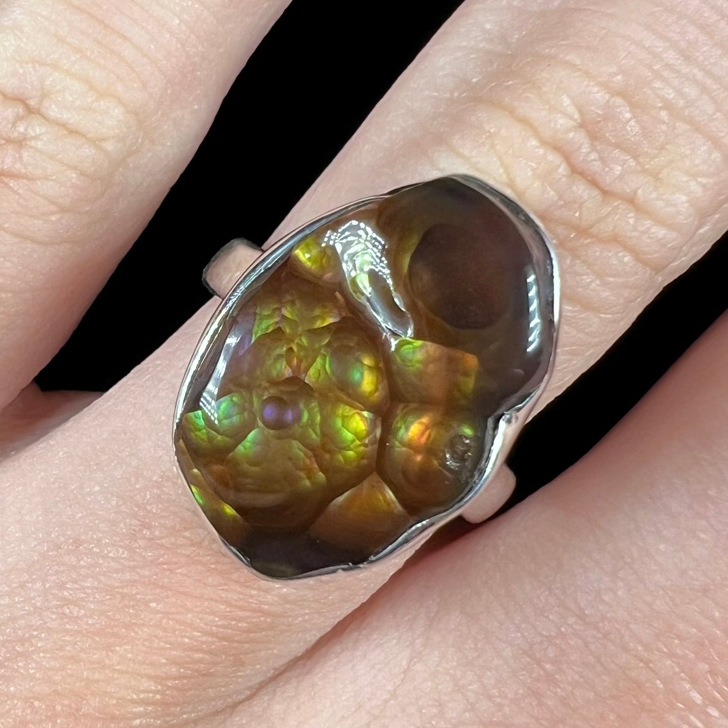 A sterling silver Mexican fire agate ring with green and purple iridescence, shown close-up on a finger.