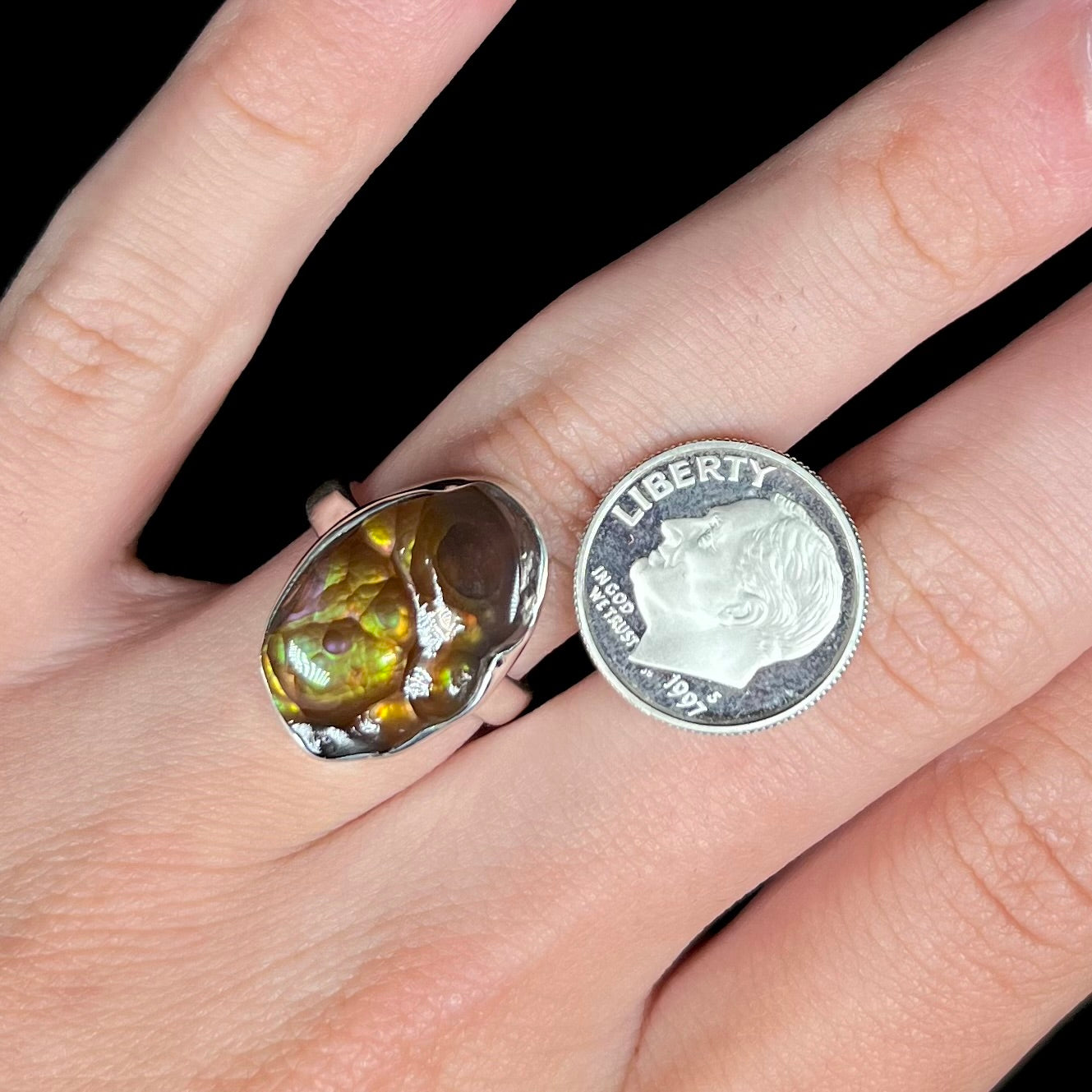 A sterling silver Mexican fire agate ring with green iridescence worn on a hand next to a dime coin.