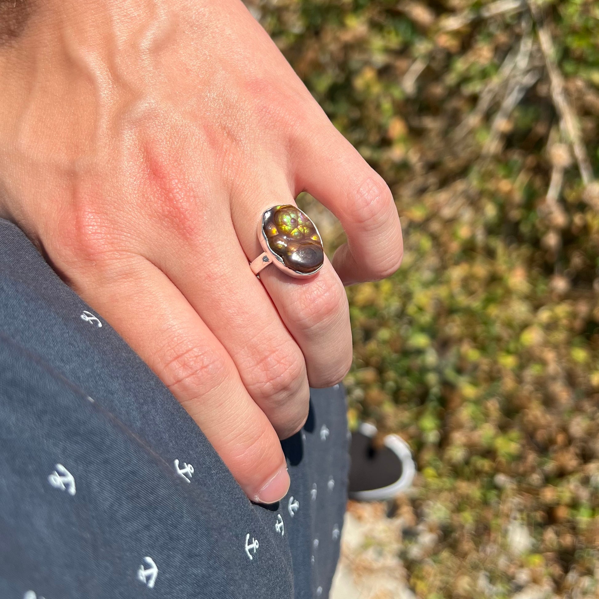 A sterling silver Mexican fire agate ring with green iridescence worn on a hand resting on a model's hip in sunlight.