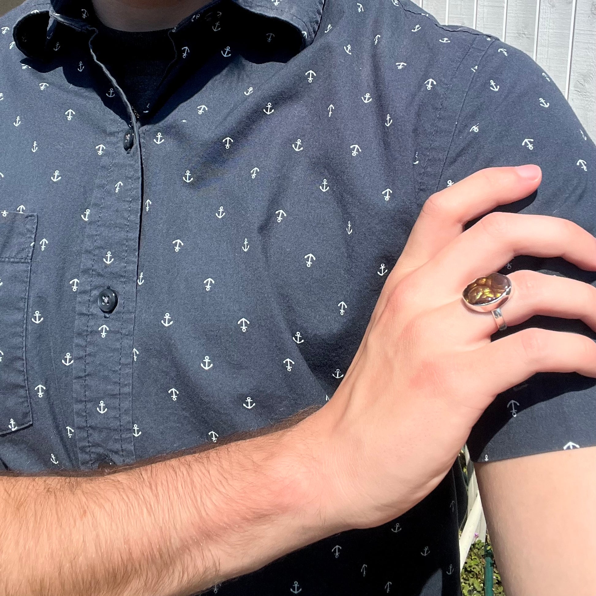 A sterling silver Mexican fire agate ring with green iridescence worn on a model's hand as it rests on his shoulder.