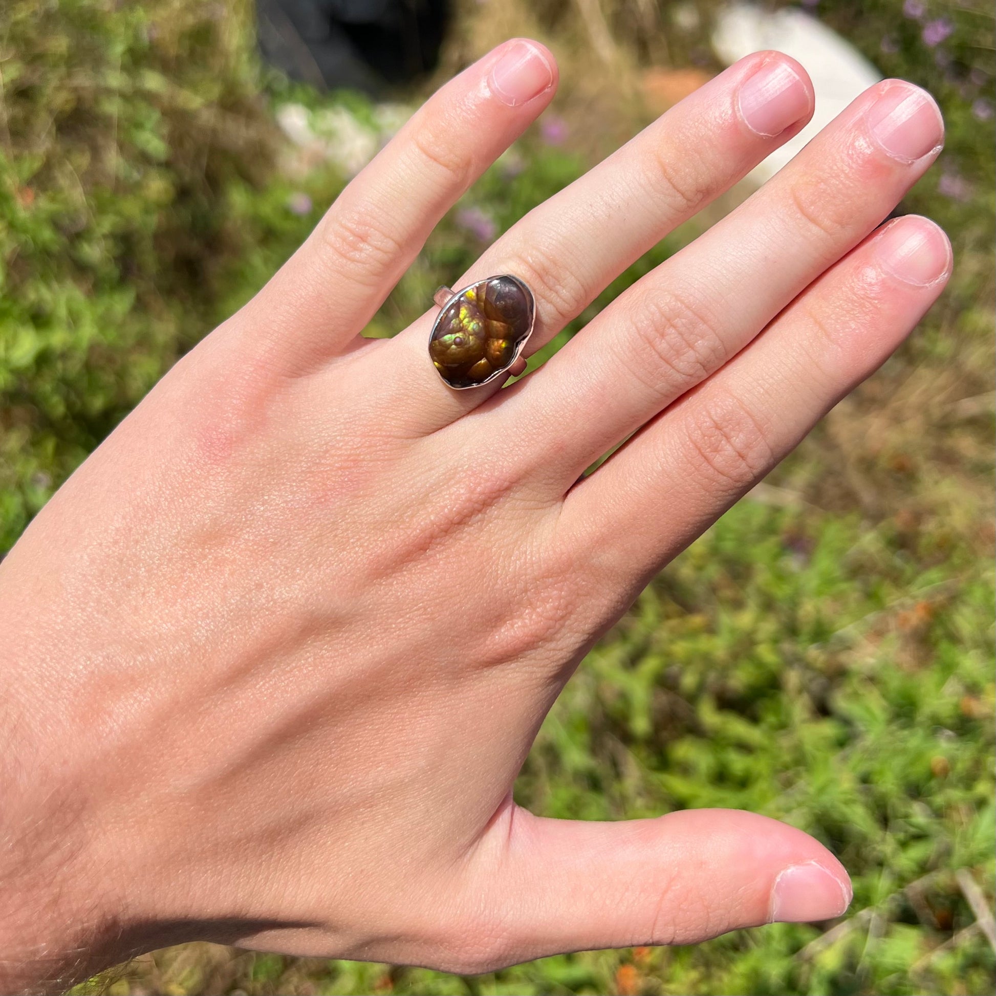 A sterling silver Mexican fire agate ring with green iridescence worn on a hand in the sunlight.