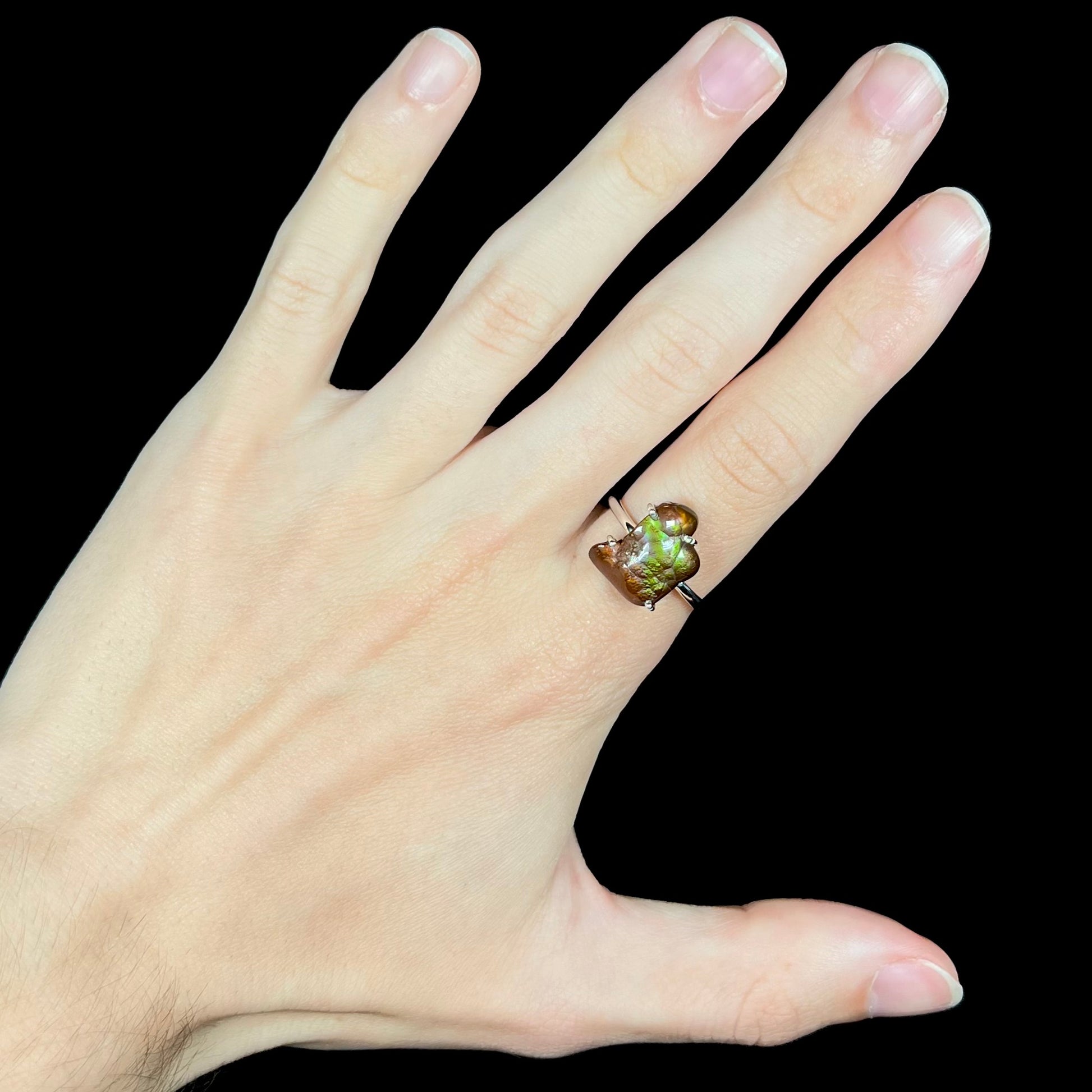 Deer Creek fire agate ring worn on hand against black background with visible green iridescence.