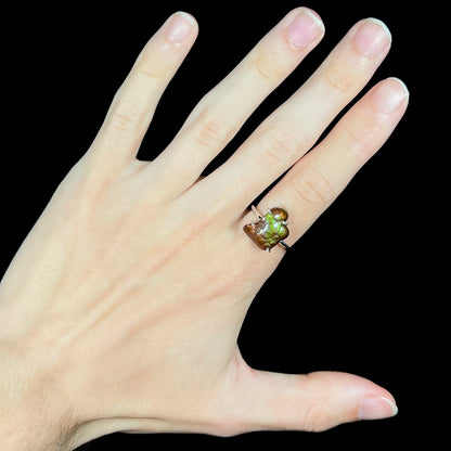 Deer Creek fire agate ring worn on hand against black background with visible green iridescence.