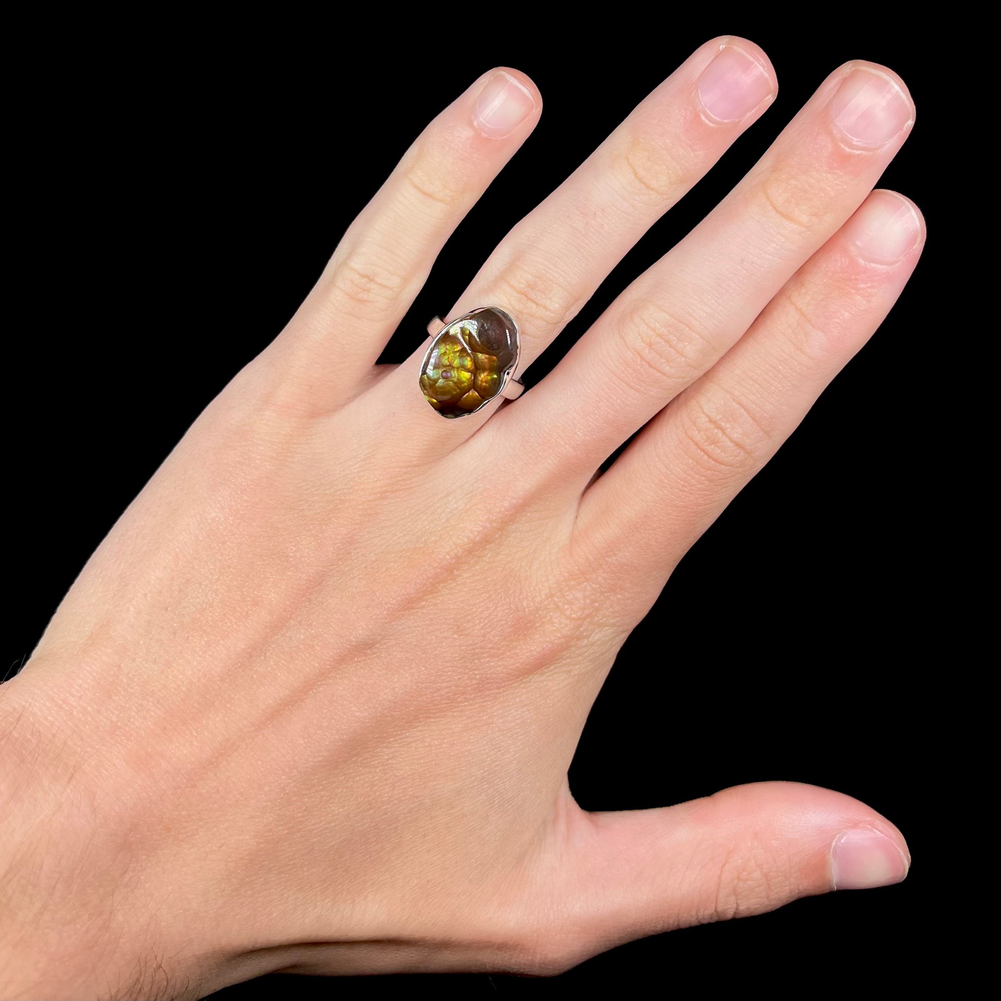 A sterling silver Mexican fire agate ring with green iridescence, worn on a hand.