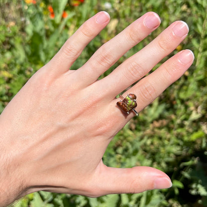 Fire agate ring worn outdoors with green iridescence visible in natural sunlight.