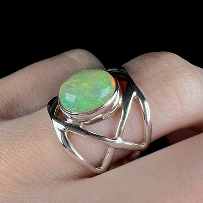 A green fire opal ring with a silver open design, worn on a finger and shown at an angle in LED lighting.