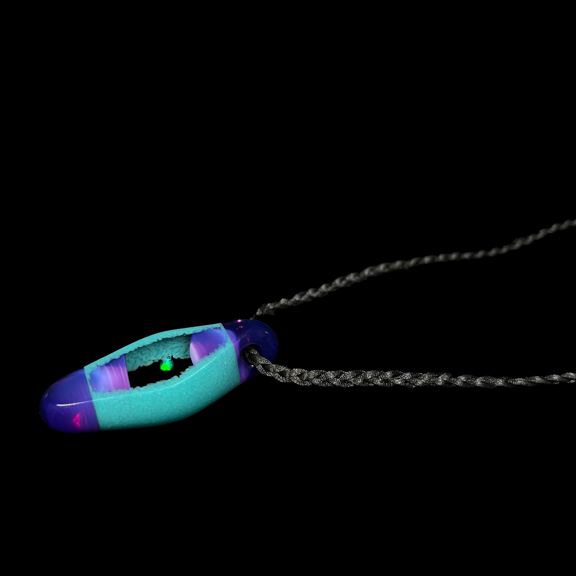 Angled view of an opal in teal and purple glass pendant, shown laying a black background.  The opal has a green flash.