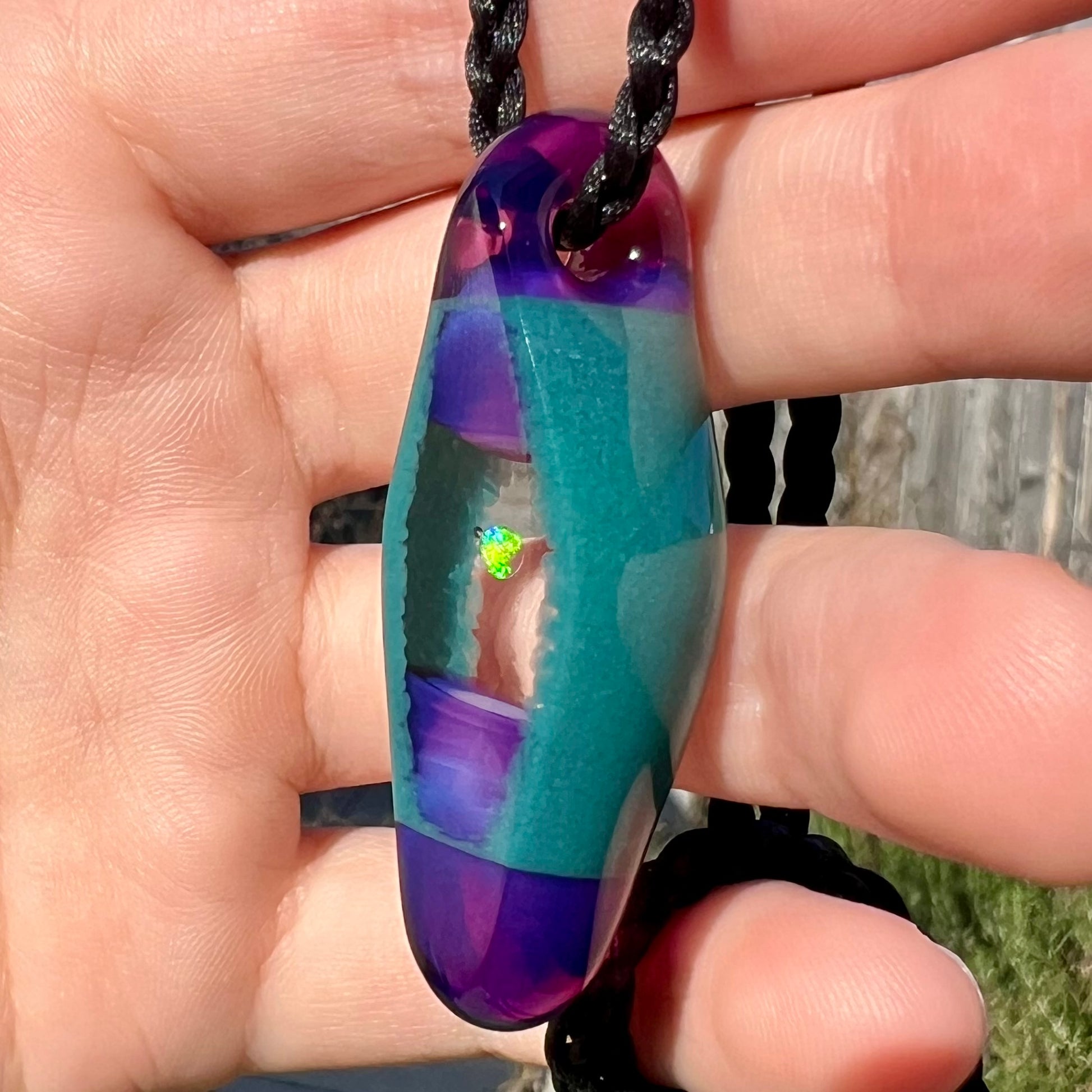 A bright green flash of color seen in a lab opal in boro glass necklace, shown close-up from an angle in the sunlight.