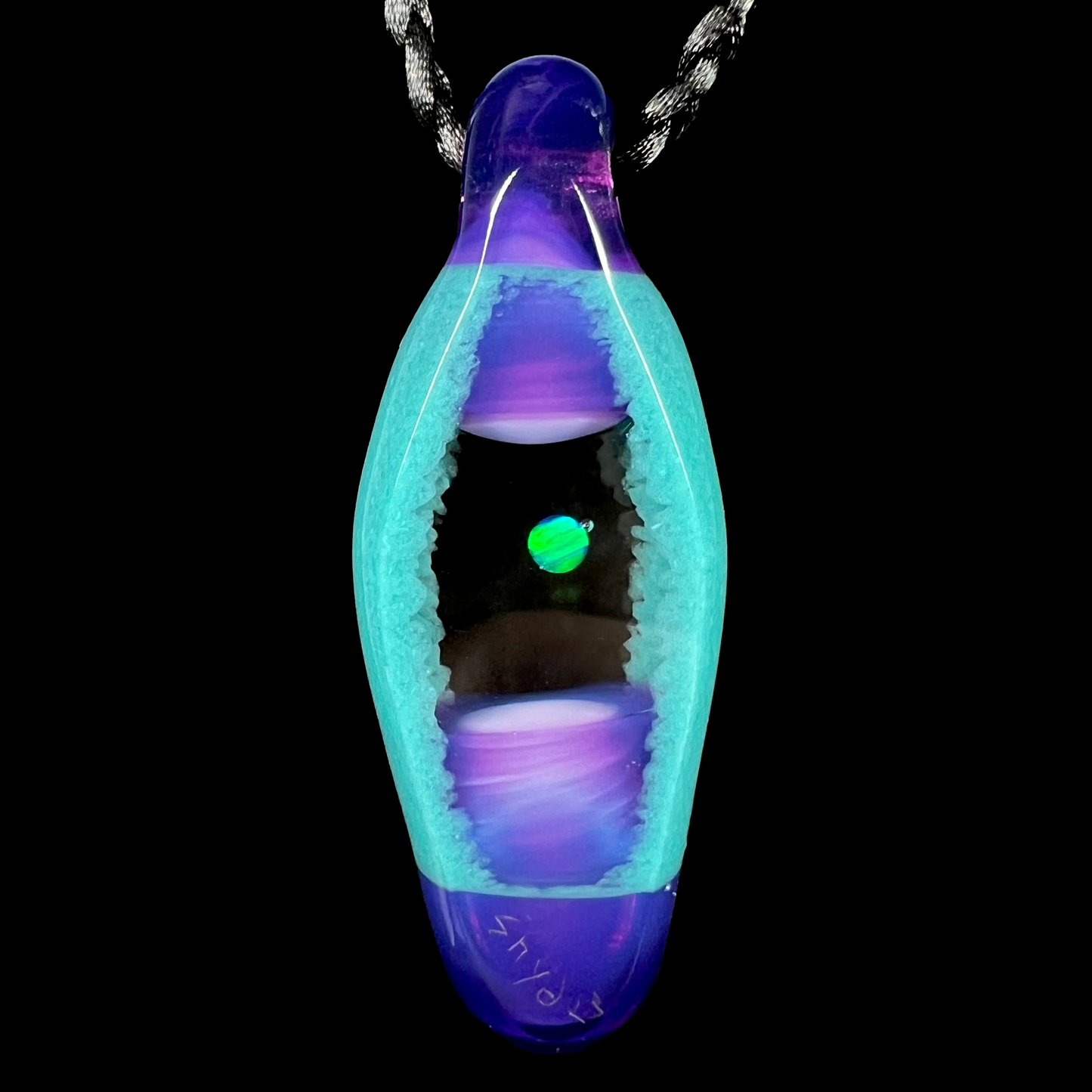 Back side of a green lab-created opal and glass pendant, shown on a black cord against a black backdrop.
