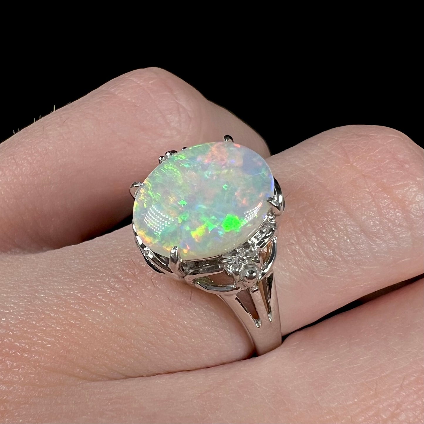 A platinum opal and diamond ring on a finger.  The opal shows green colors.