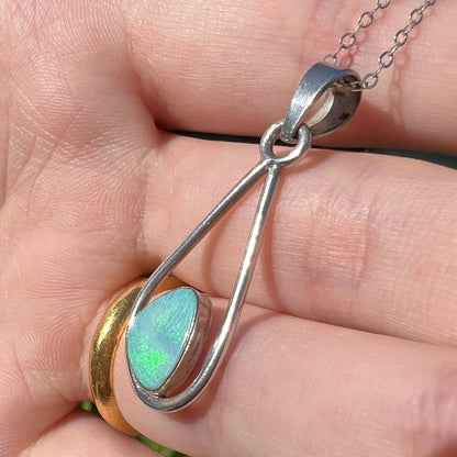 Sterling silver opal doublet necklace held by a hand at an angle in sunlight shown close-up.  The opal has soft green play of color.