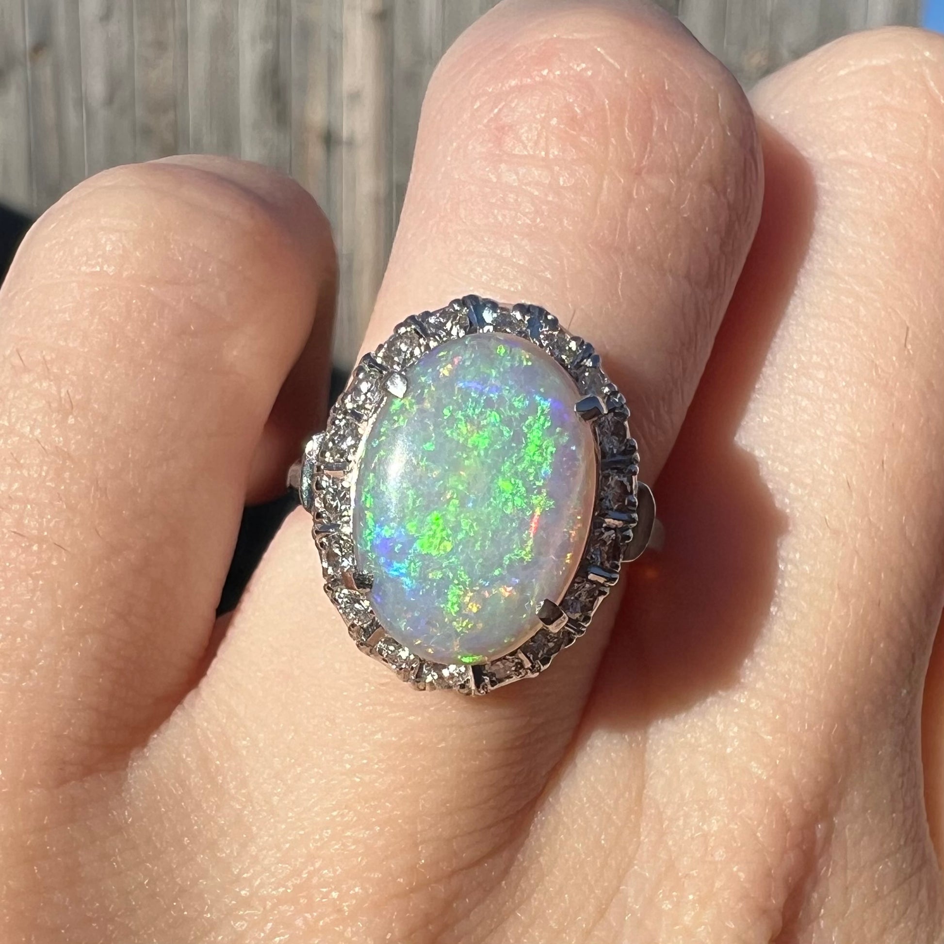 A green opal and diamond halo enggagement ring on a finger in the sunlight.