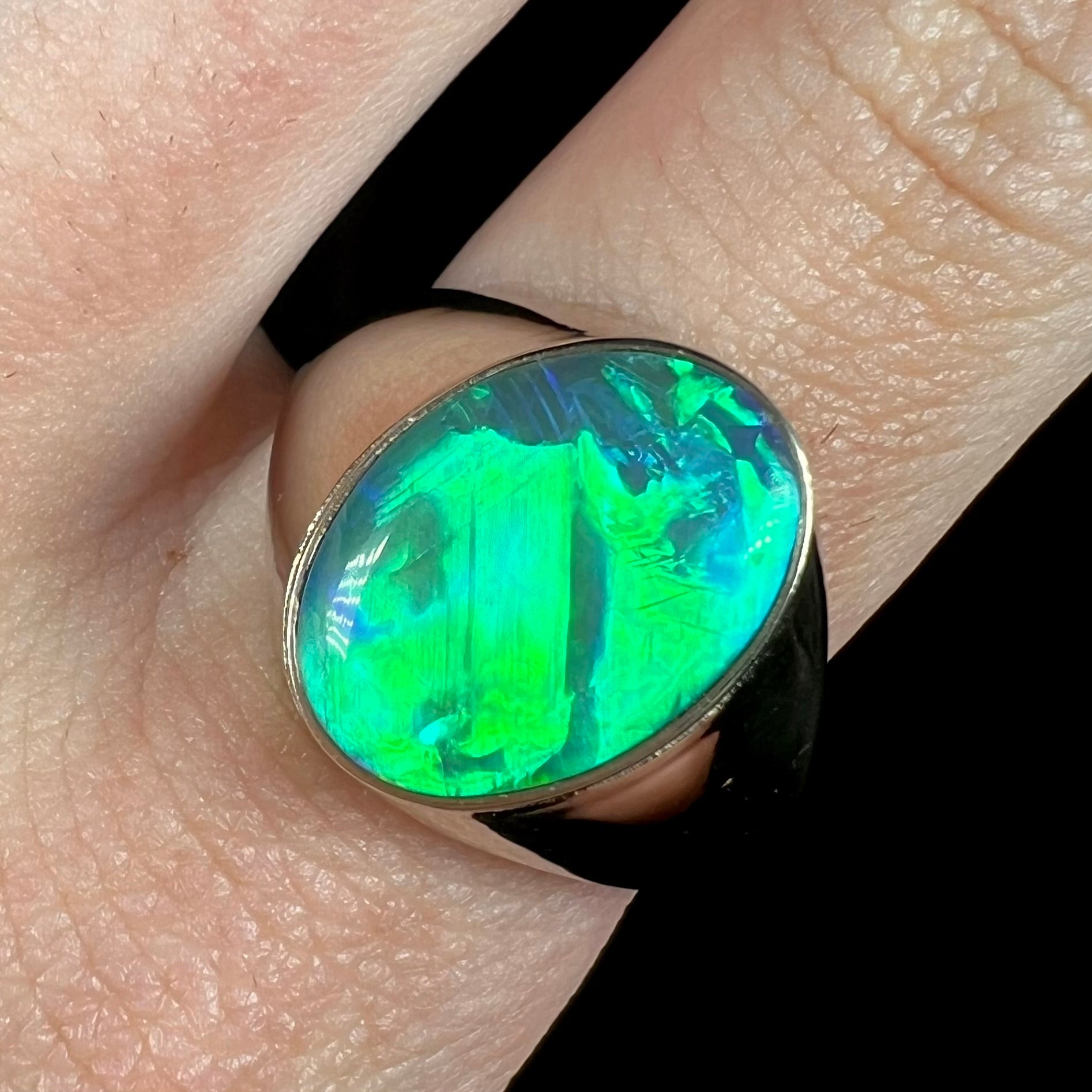 Close-up of oval shaped green Australian opal men's ring in white gold on finger